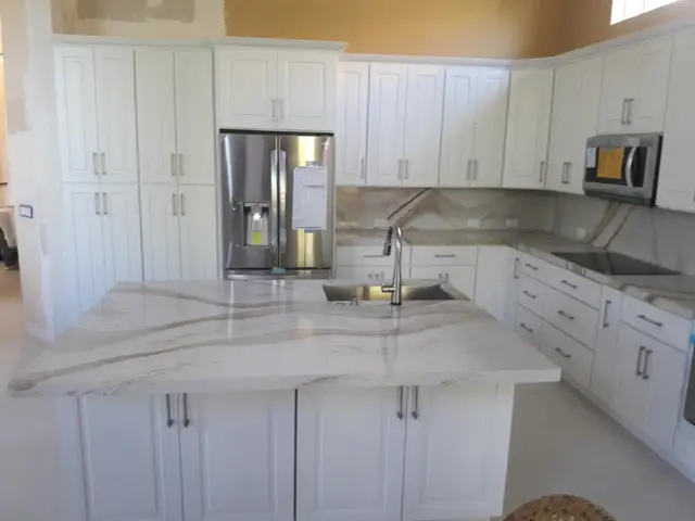 White kitchen with marble waterfall island and stainless refrigerator